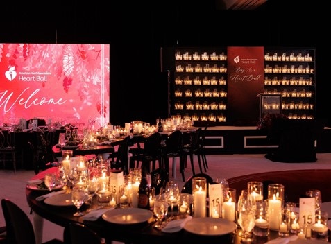 Empty ballroom with candles lit on tables and a wall of lit candles behind the podium on stage.